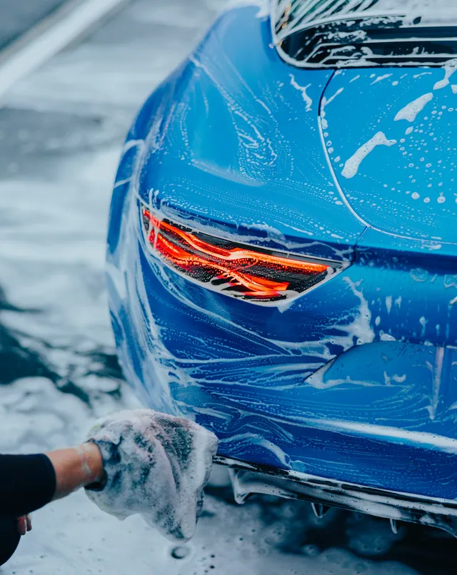 A wash mitt working along the sill of a bright blue car covered in foam