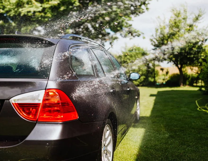 A dark wagon being rinsed with a hose on a sunny lawn