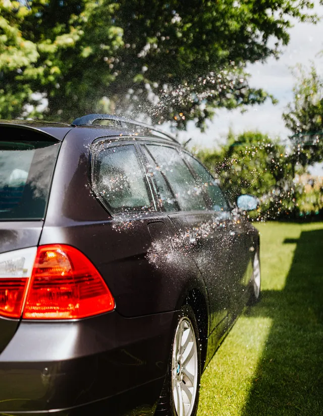 Water spraying across the rear of a parked wagon in a leafy garden