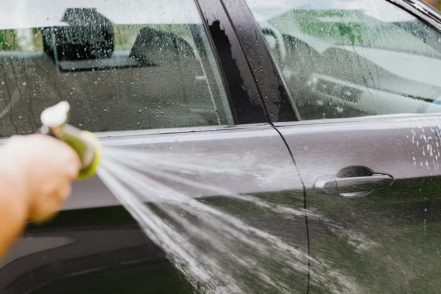 A garden hose spraying the door of a dark car