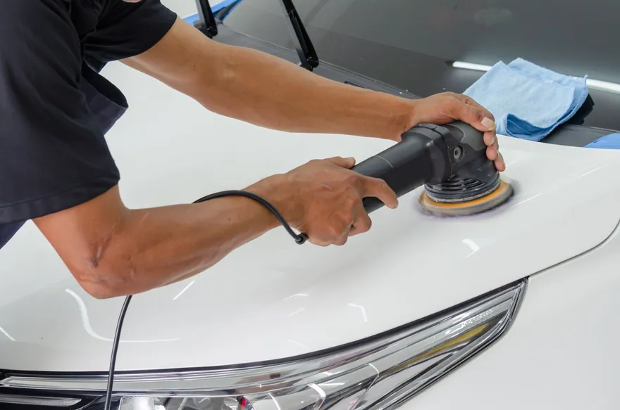 A detailer machine-polishing the hood of a white car