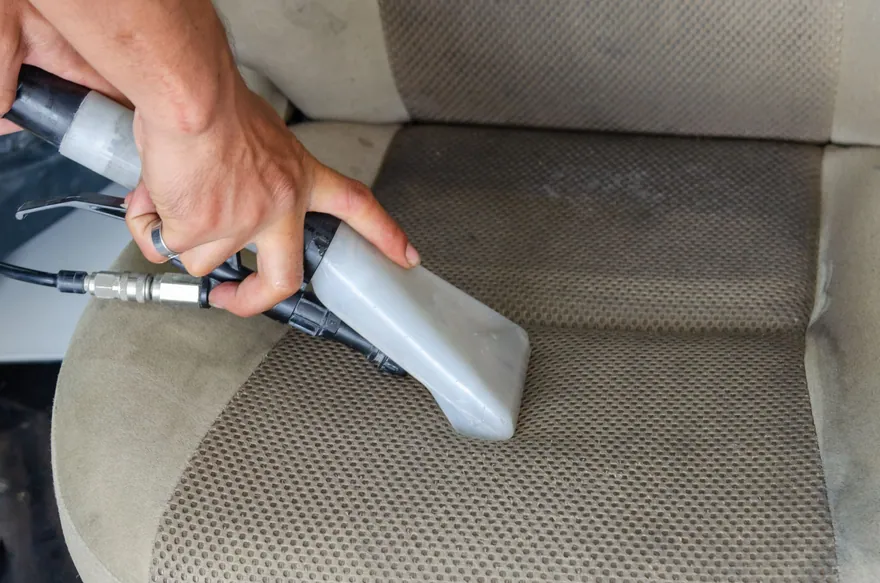 A detailer shampooing a fabric car seat with an extractor