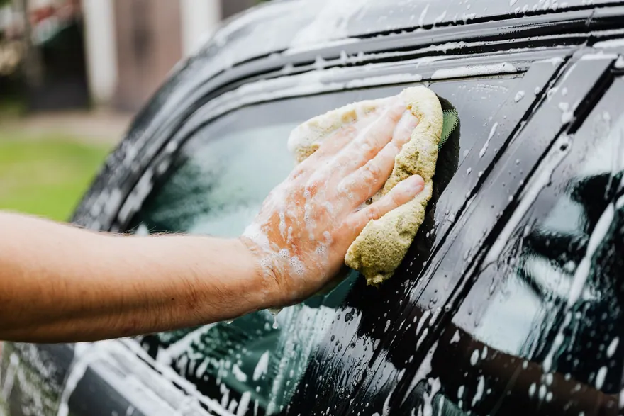 A hand washing a car window with a soapy sponge