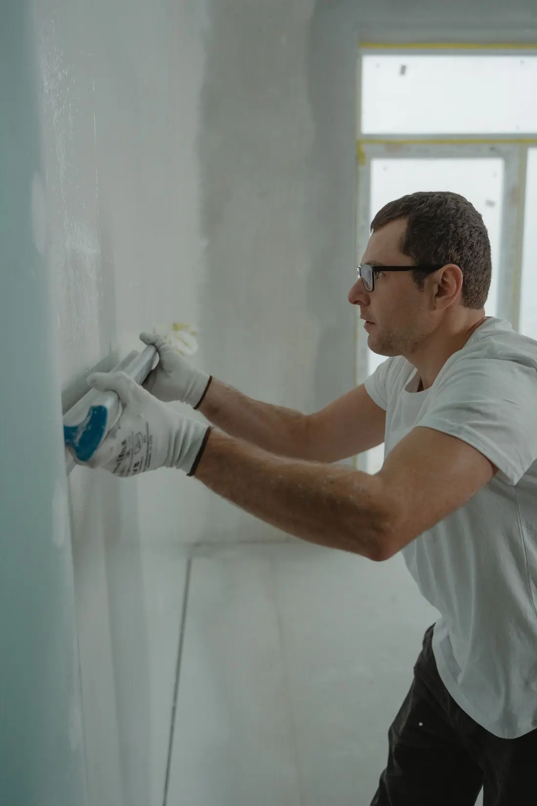 A man in work gloves smoothing a freshly finished white wall