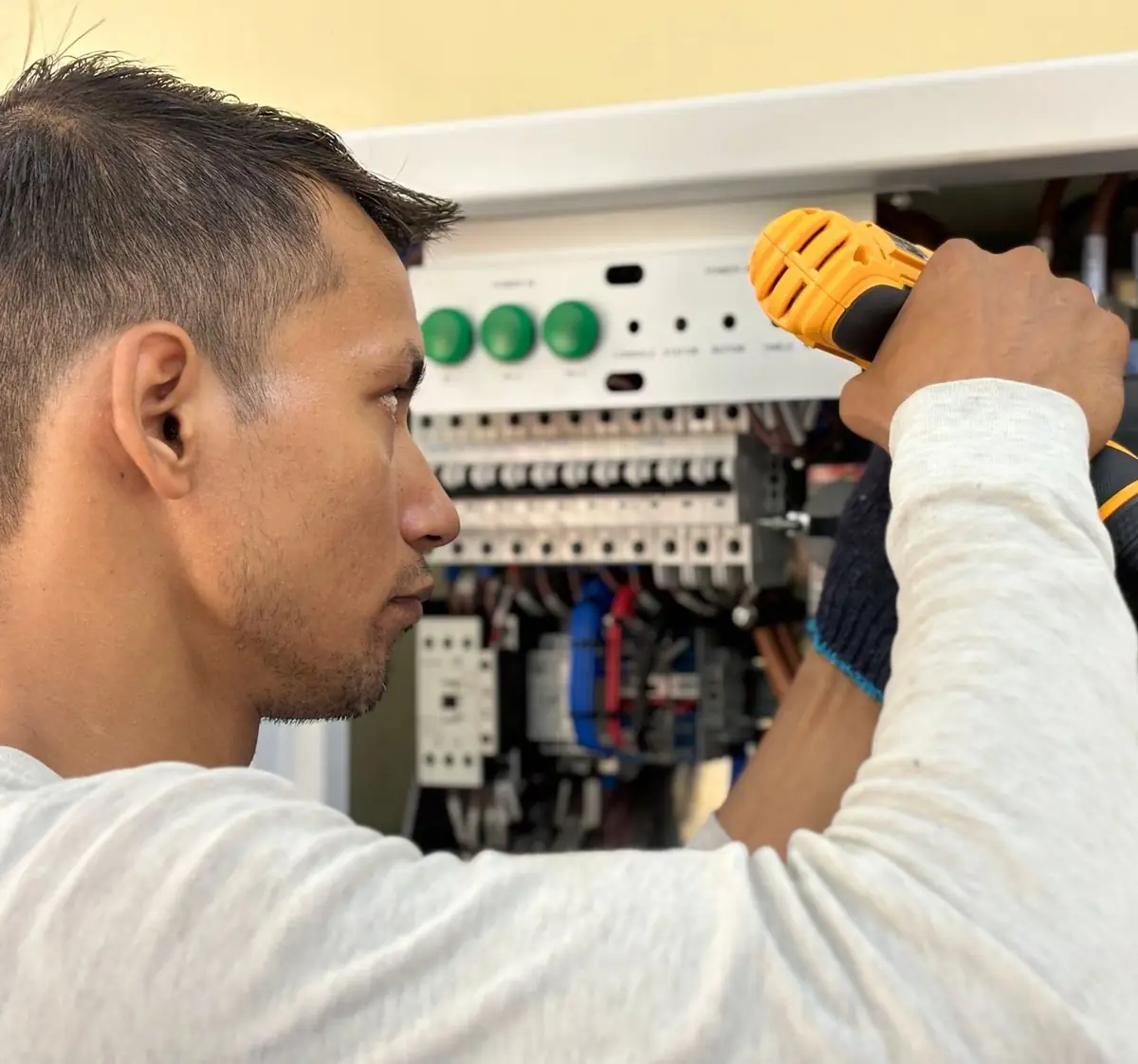 An electrician working on an open electrical panel with a cordless screwdriver