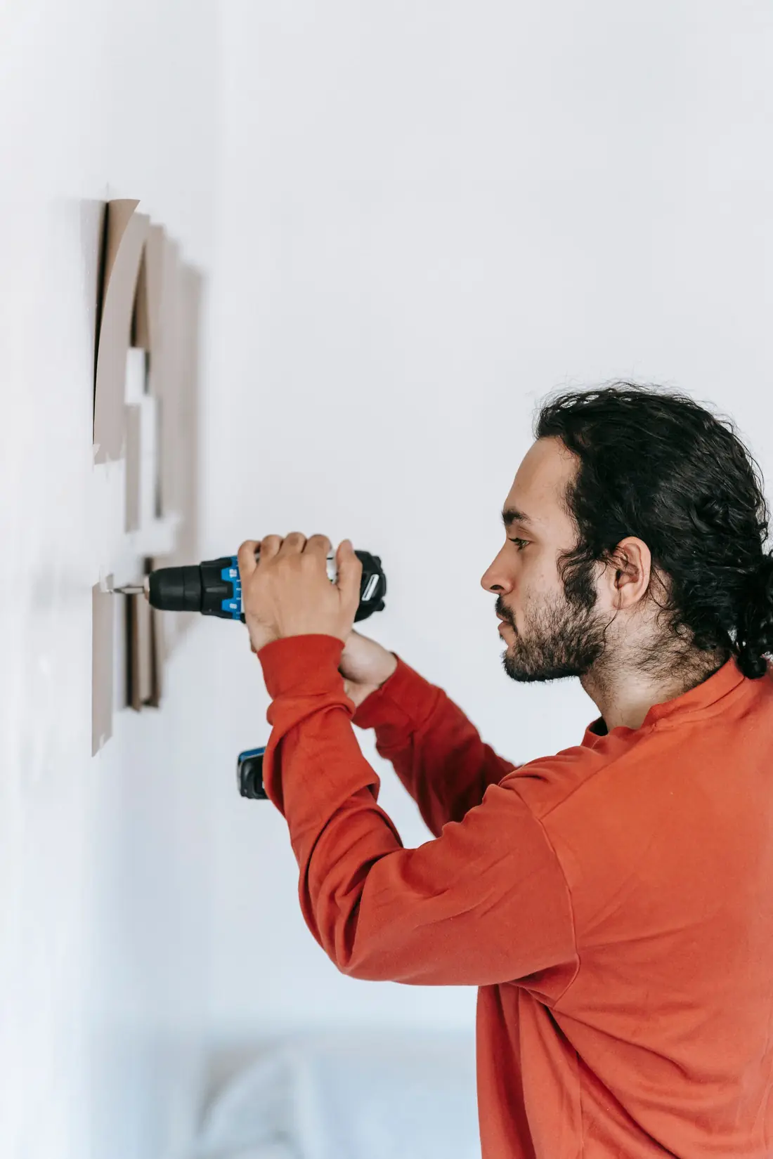 A handyman in a red shirt drilling into a white wall