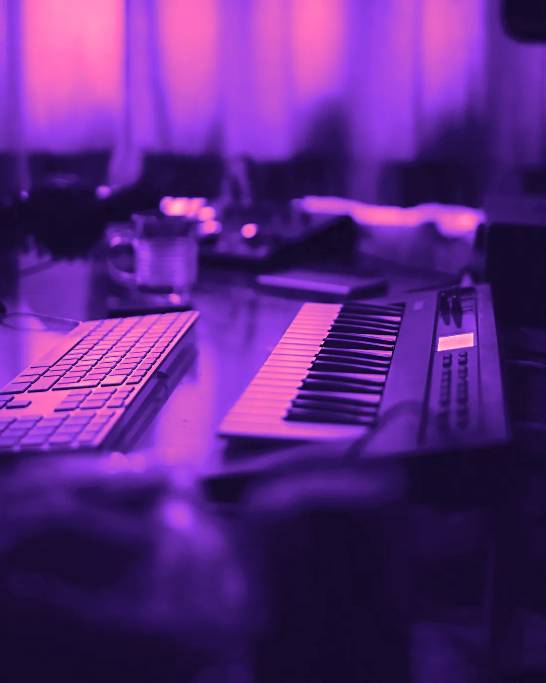 A MIDI keyboard beside a computer keyboard on a desk at night