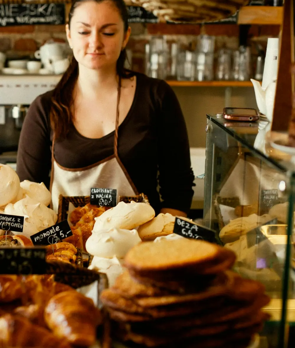 A baker behind her counter, with baskets of croissants, meringues and cookies in front of her