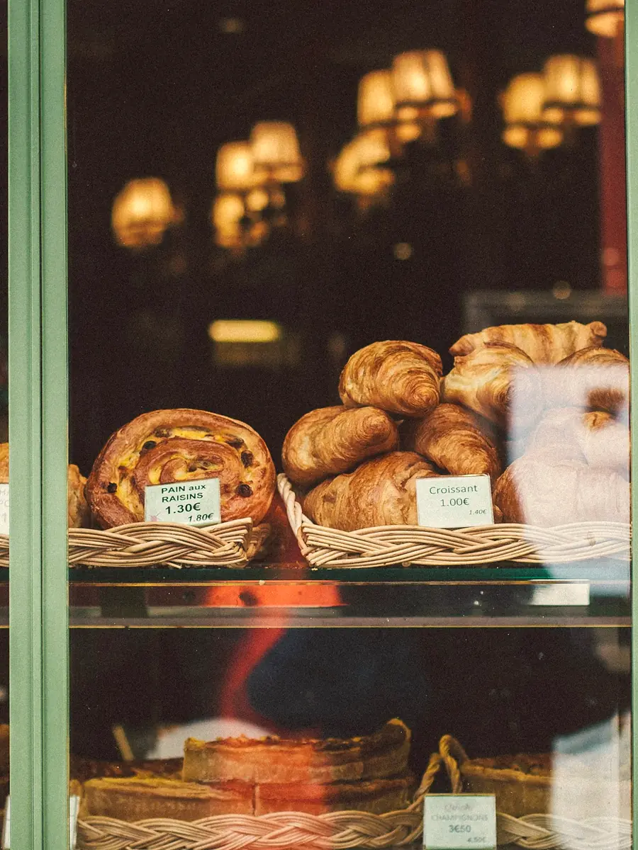 Croissants and pastries in a bakery window at dusk, with warm lamps glowing inside