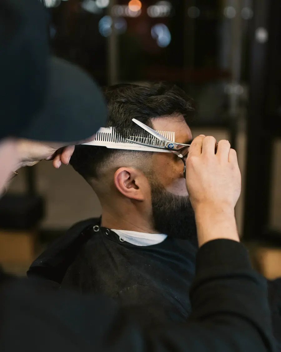 A barber trimming a client’s hair with scissors and a comb