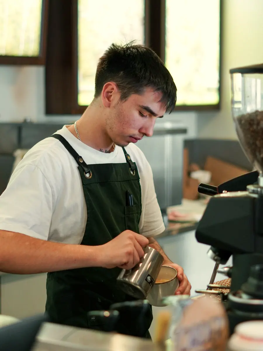 A barista in an apron pouring steamed milk into a cup