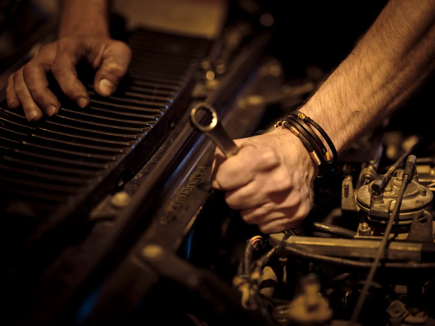 A mechanic’s hands tightening a bolt in an engine bay with a wrench