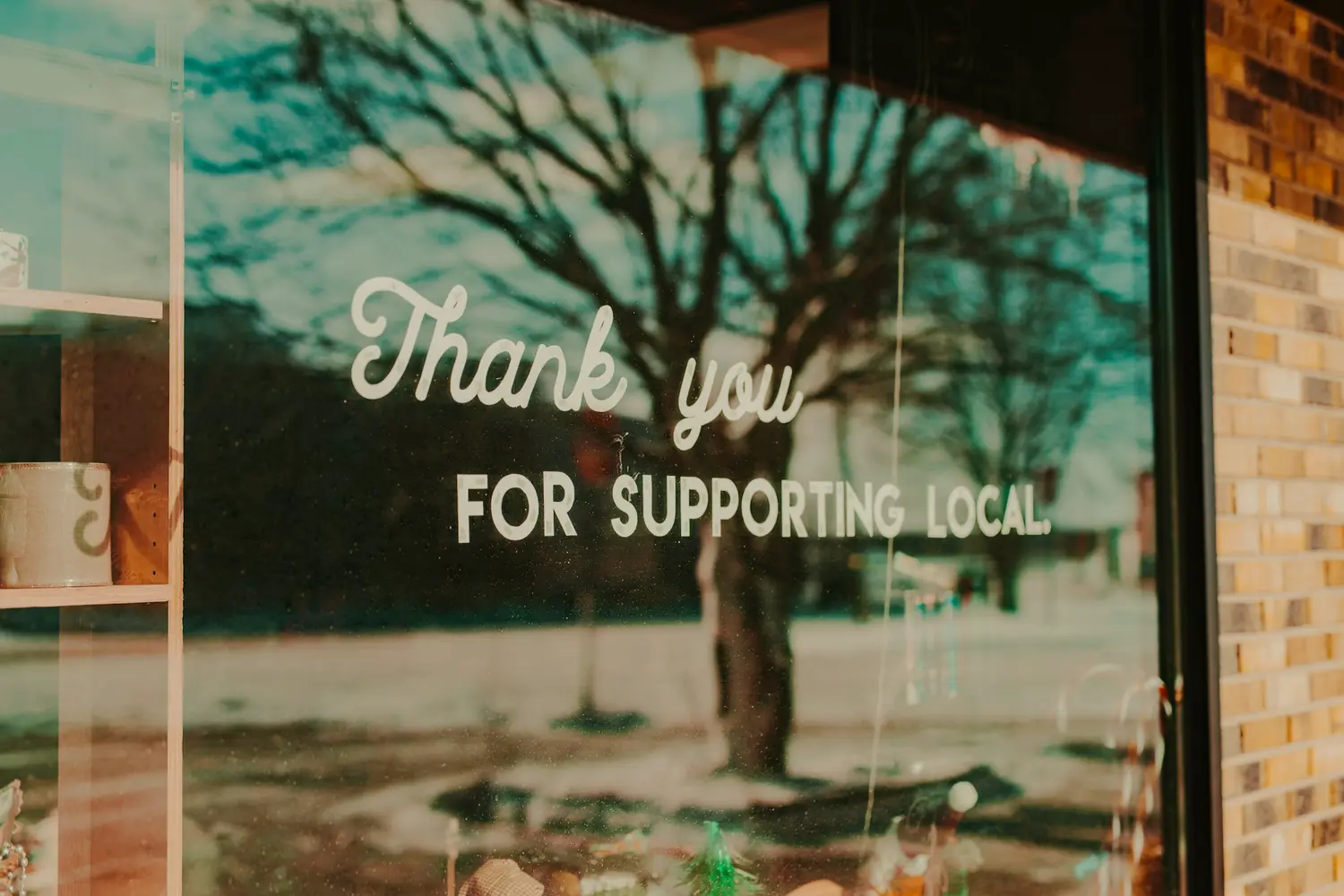 A shop window with the words Thank you for supporting local lettered on the glass, reflecting a winter street