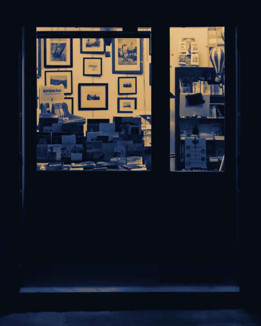 A small shop front at night, its window lit from inside on a dark street.